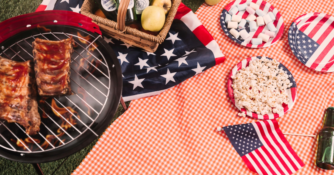 Backyard 4th of July BBQ setup featuring rustic outdoor furniture, cozy seating areas, string lights, and patriotic decor for a summer gathering.