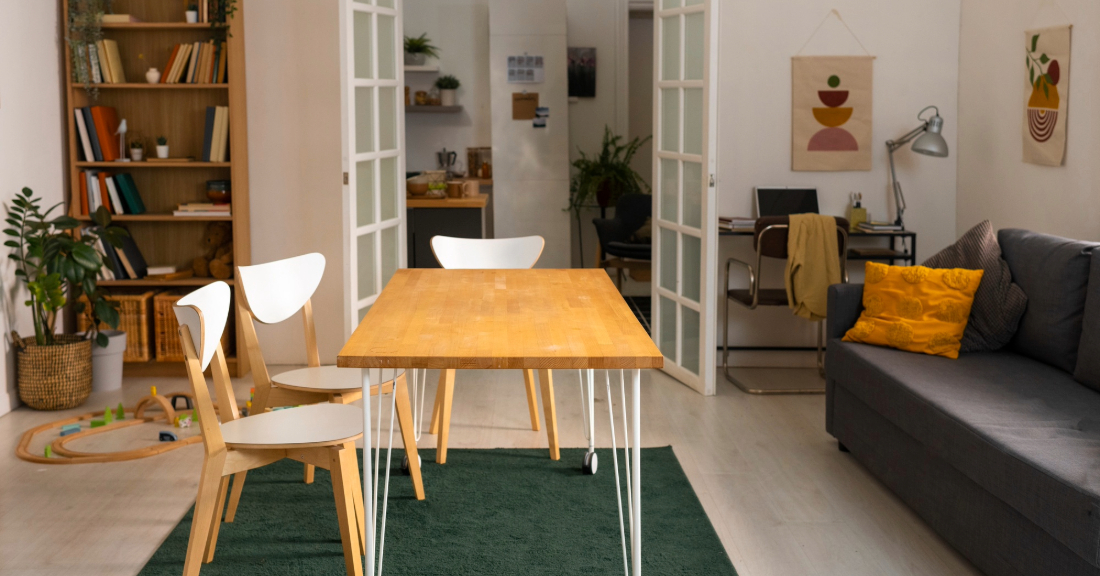 A cozy, stylish apartment living room with compact furniture, vertical shelving, and a bold yellow accent chair in a sunlit space.