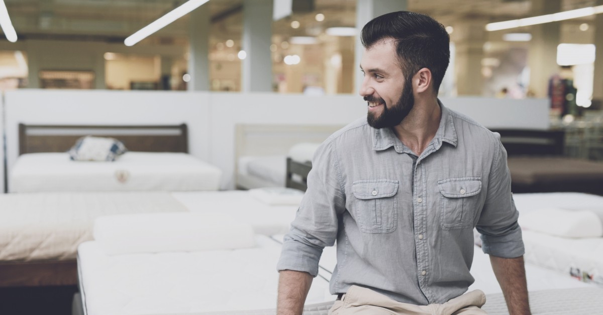 Man sitting on a mattress inside of a furniture store.